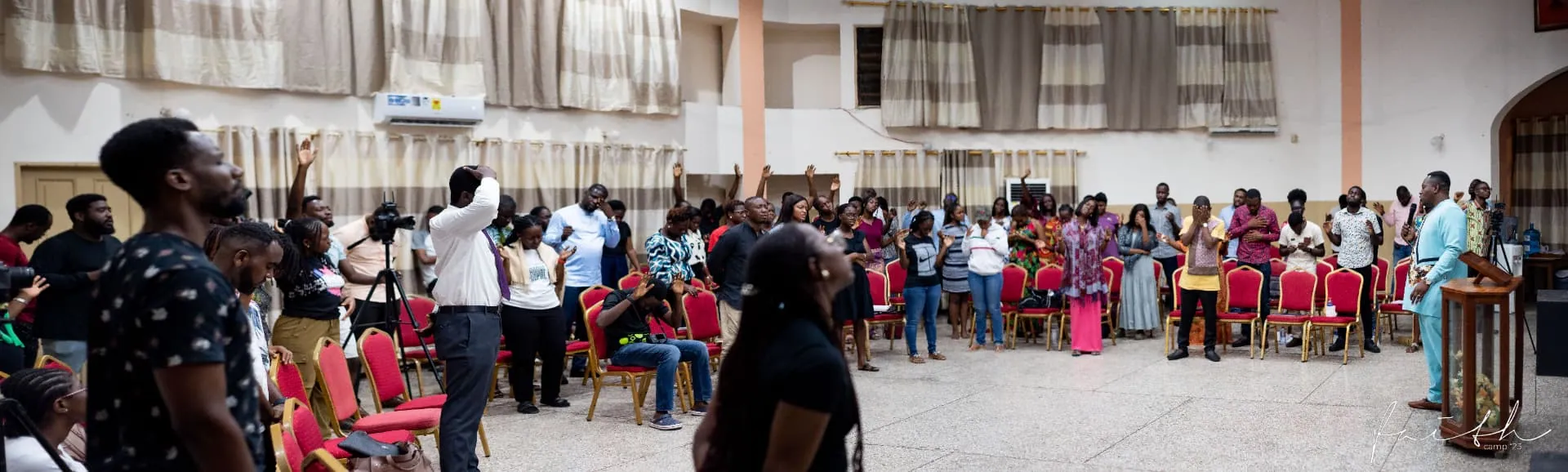 The Faith Camp hall full of people worshipping with hands raised